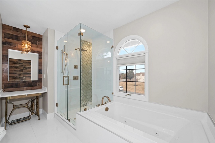 A finished primary bathroom with a frameless shower and a tub under an arched window